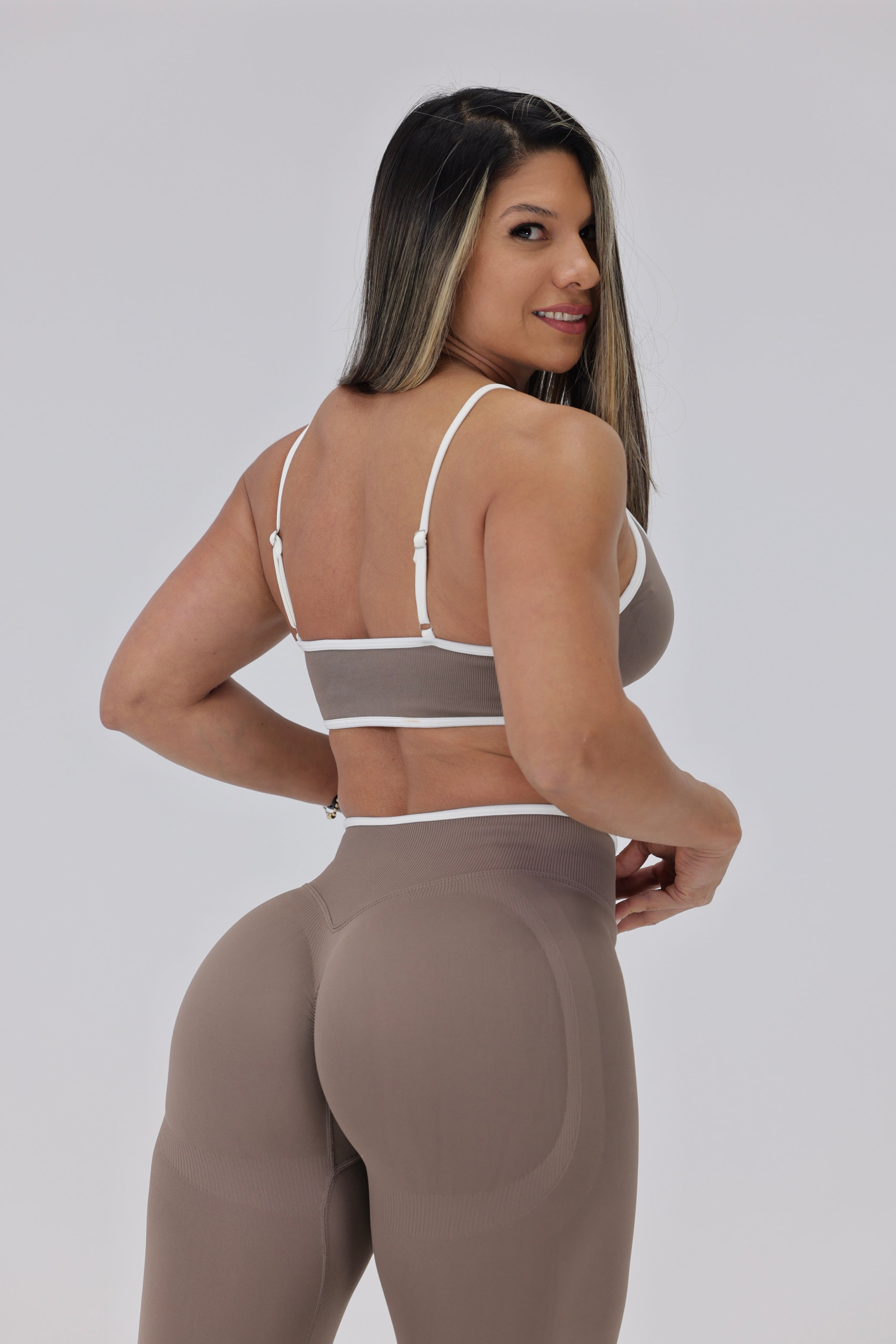 Woman wearing a beige sports bra and leggings on a plain background